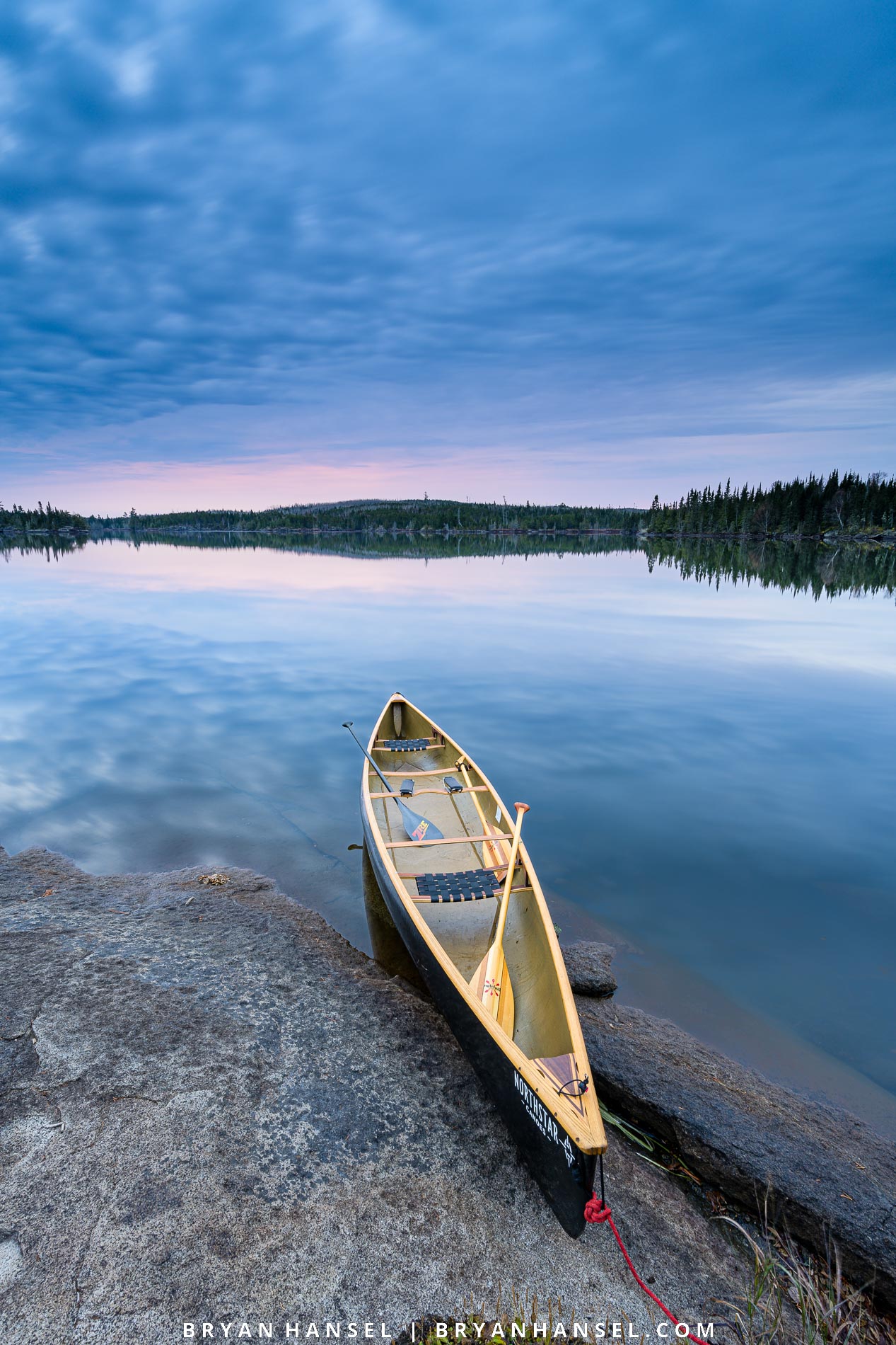 canoe on shore pointing towards sunrise under blue clouds reflecting in the blue water