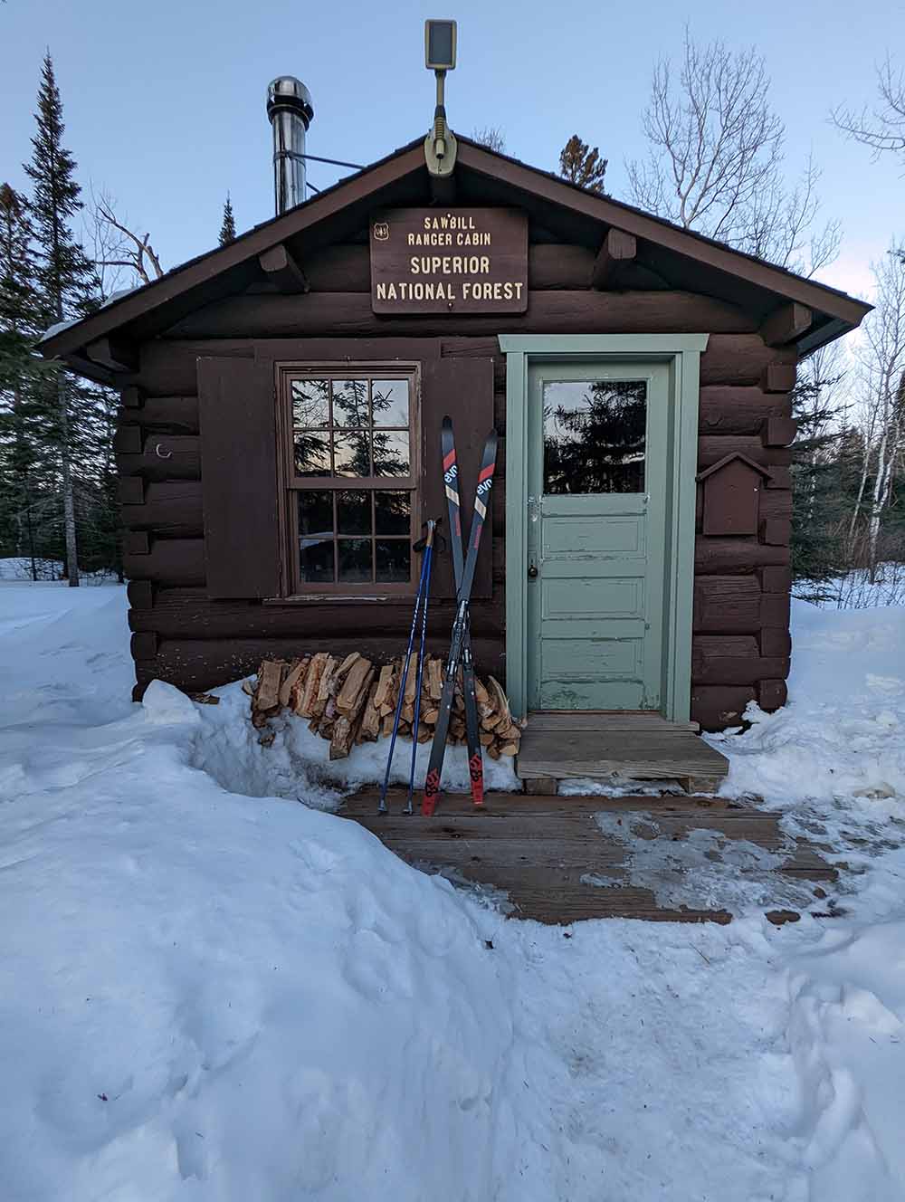 A photo of skis up against a small brown ranger station cabin.