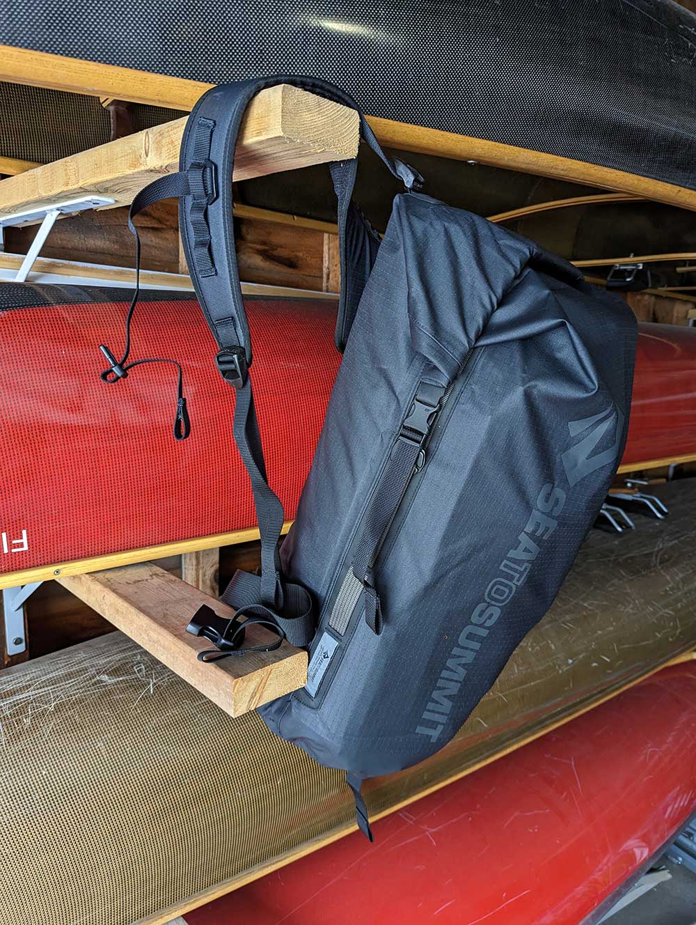 The Sea to Summit Big River Dry Backpack fully loaded and hanging on a hook by four canoes.