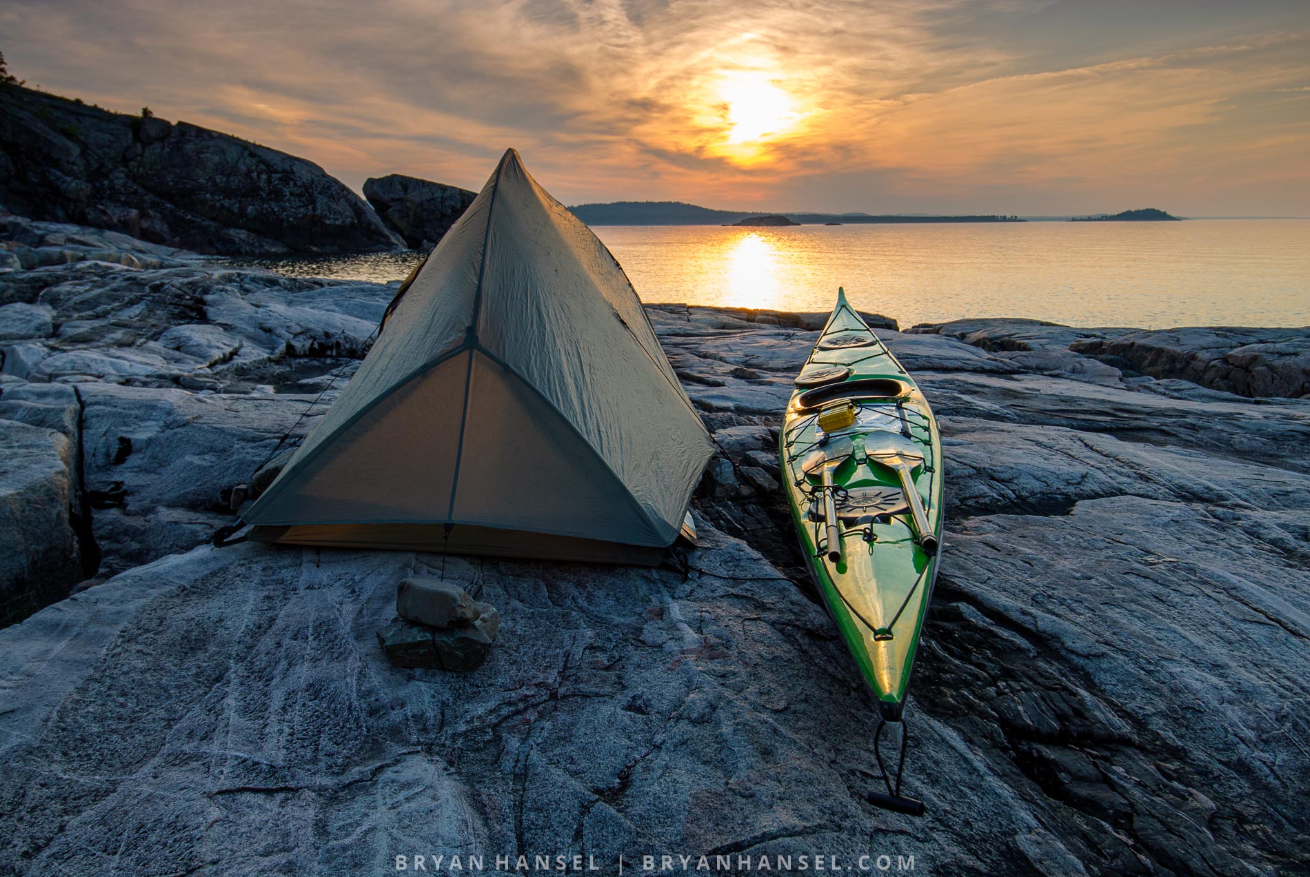 a kayak next to a tent on a rocky Lake Superior shore at sunset