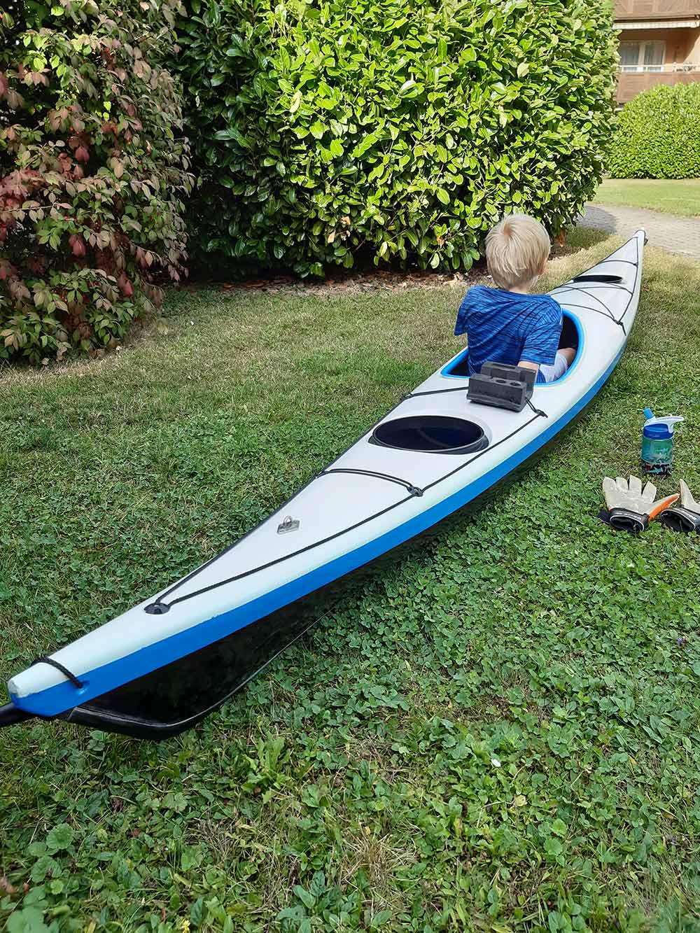 a kid sitting in a white and blue kayak on grass