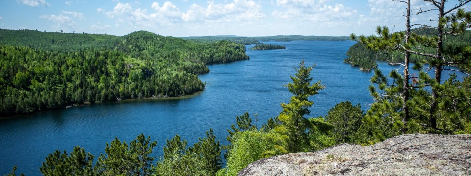 A photo of a bright blue lake in the Boundary Waters Canoe Area Wilderness surrounded by a green Boreal forest.
